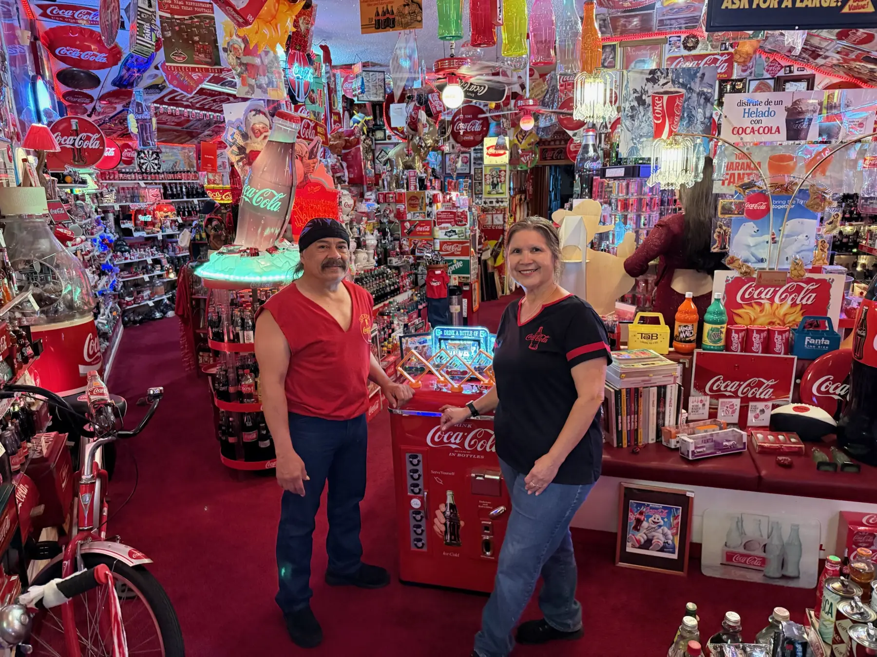 Bardo and Olga Cuellar standing in their Coca-Cola room, covered floor to ceiling in memorabilia
